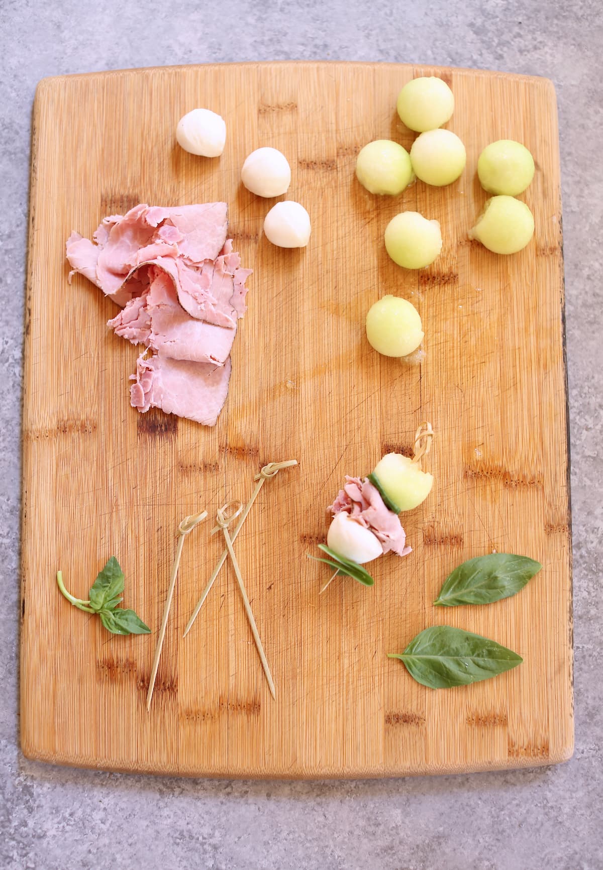 a cutting board of melon ball appetizer ingredients.