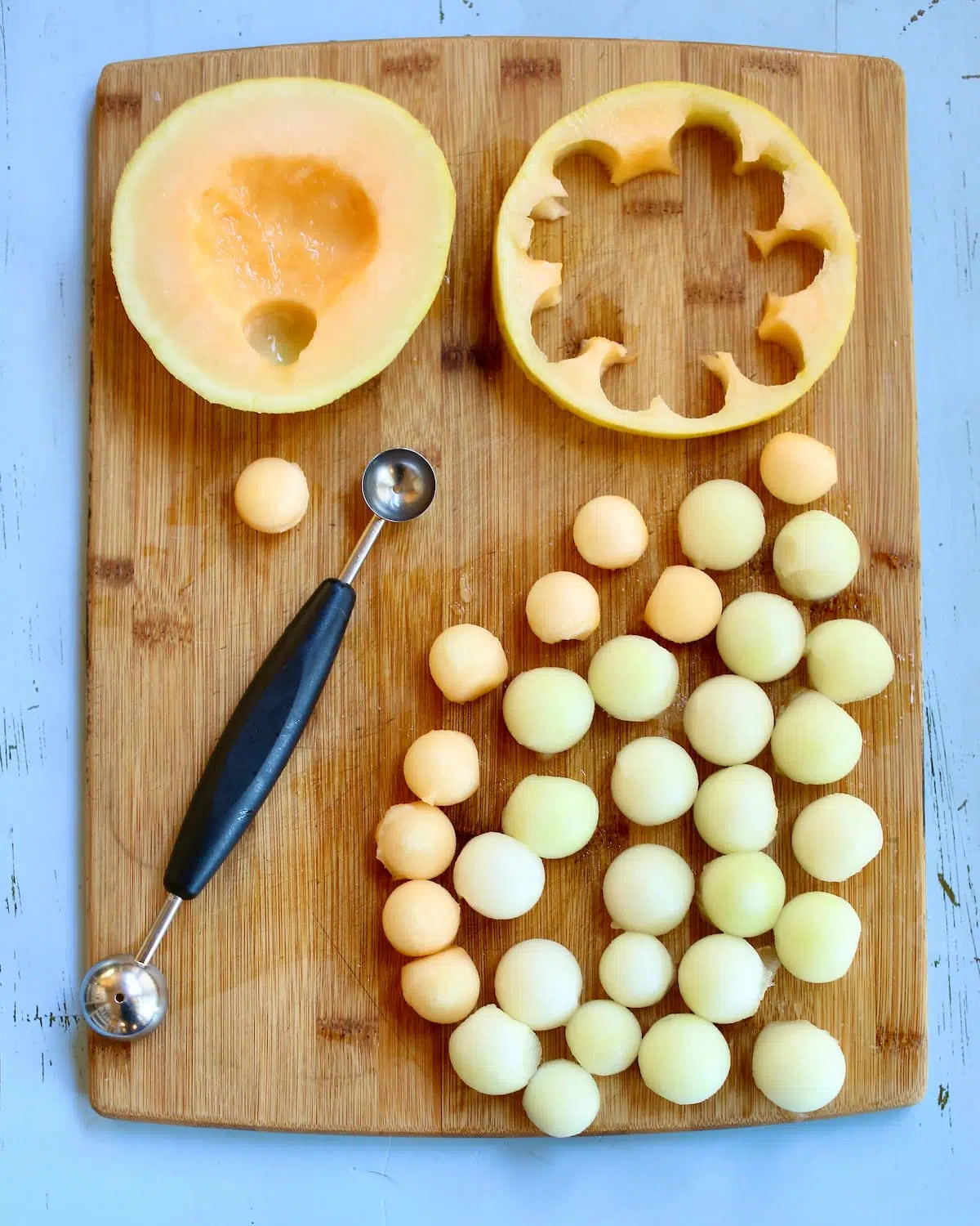 a cutting board with melon balls cut out and a melon baller.