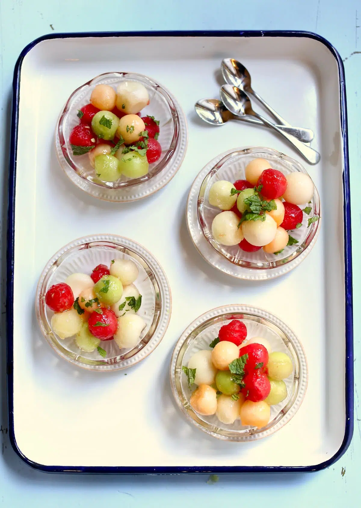 four small glass bowls on melon ball salad.