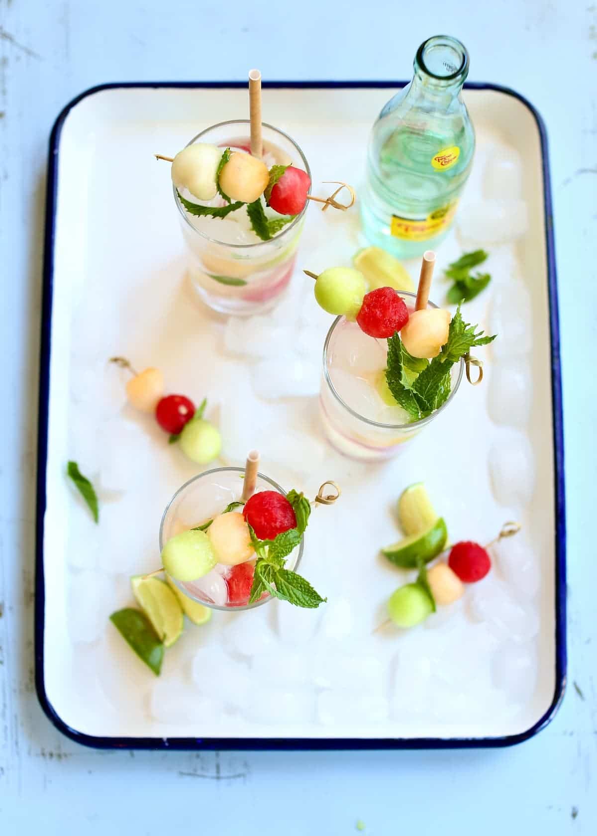 a white tray of drinks with melon balls in them.