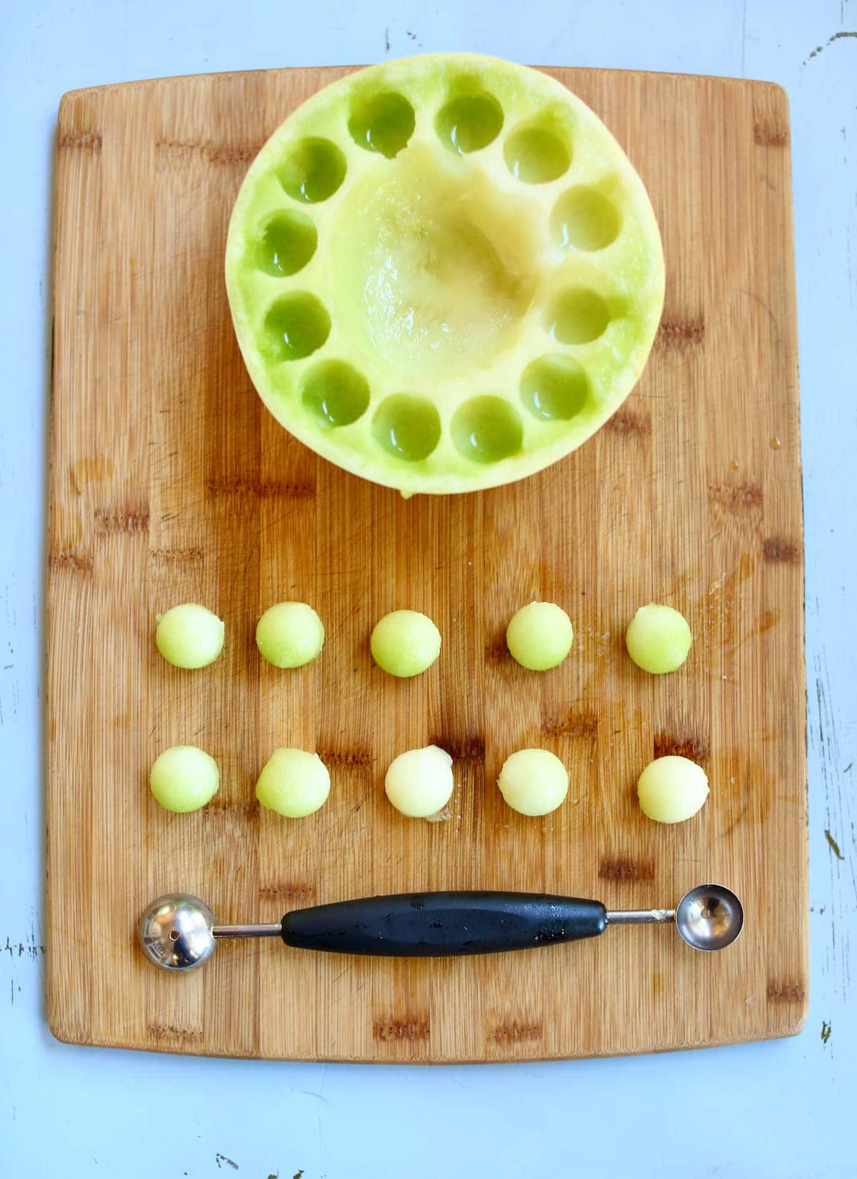 a cutting board with a tray of melon balls and melon baller.