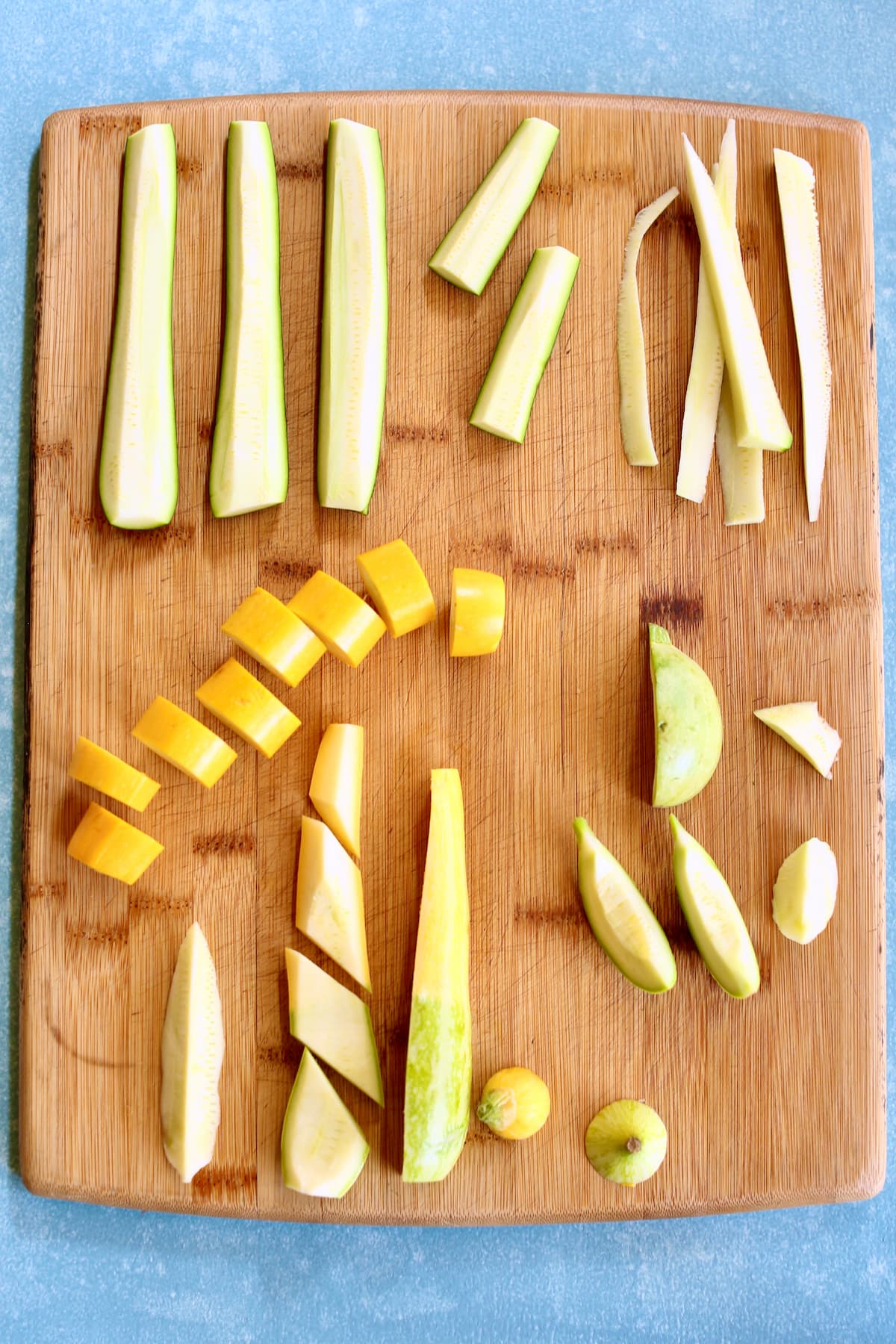 a wooden cutting board with different zucchini and squash and their knife cuts.