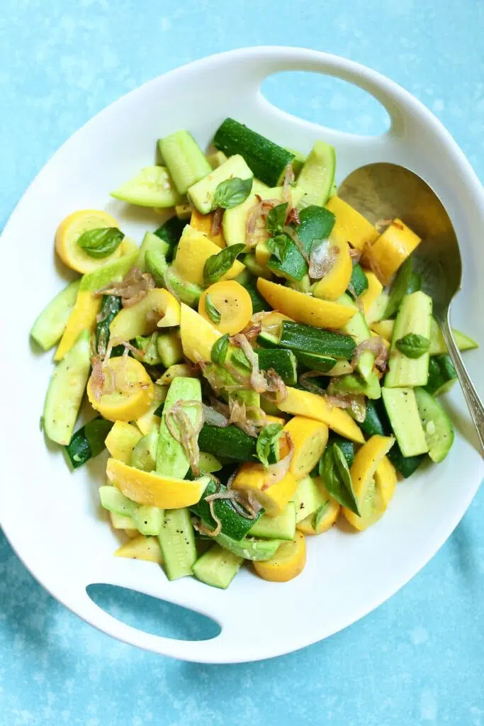 a white serving plate with sauteed zucchini.