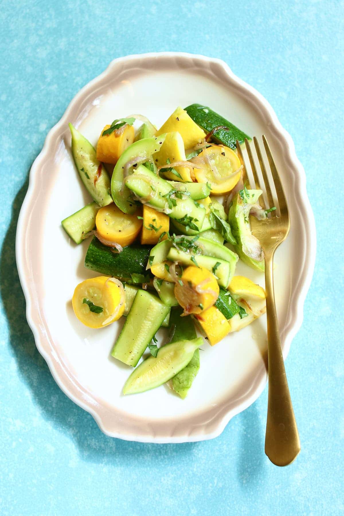 a small white plate of zucchini and a gold fork.
