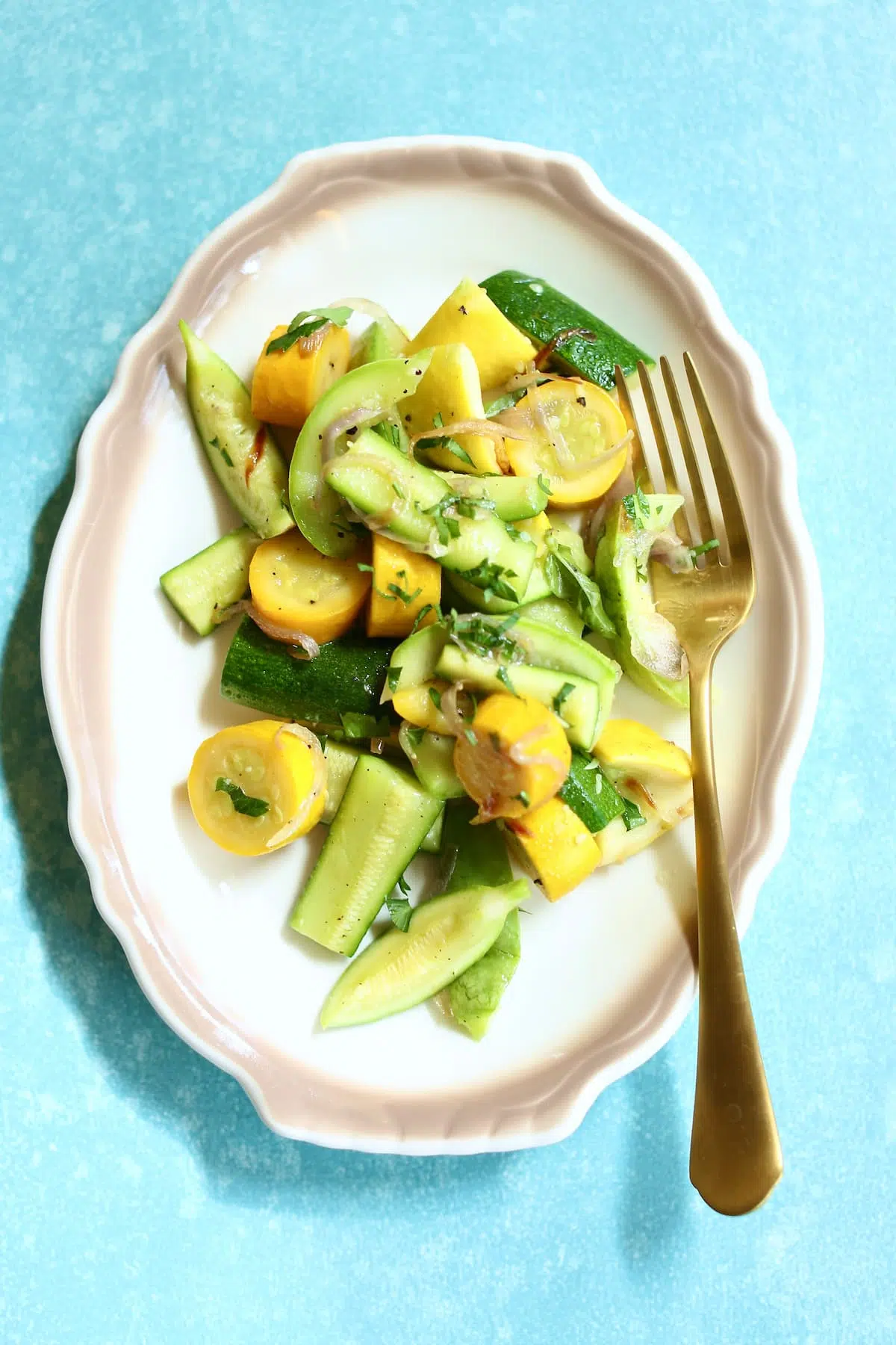 a small white plate of zucchini and a gold fork.