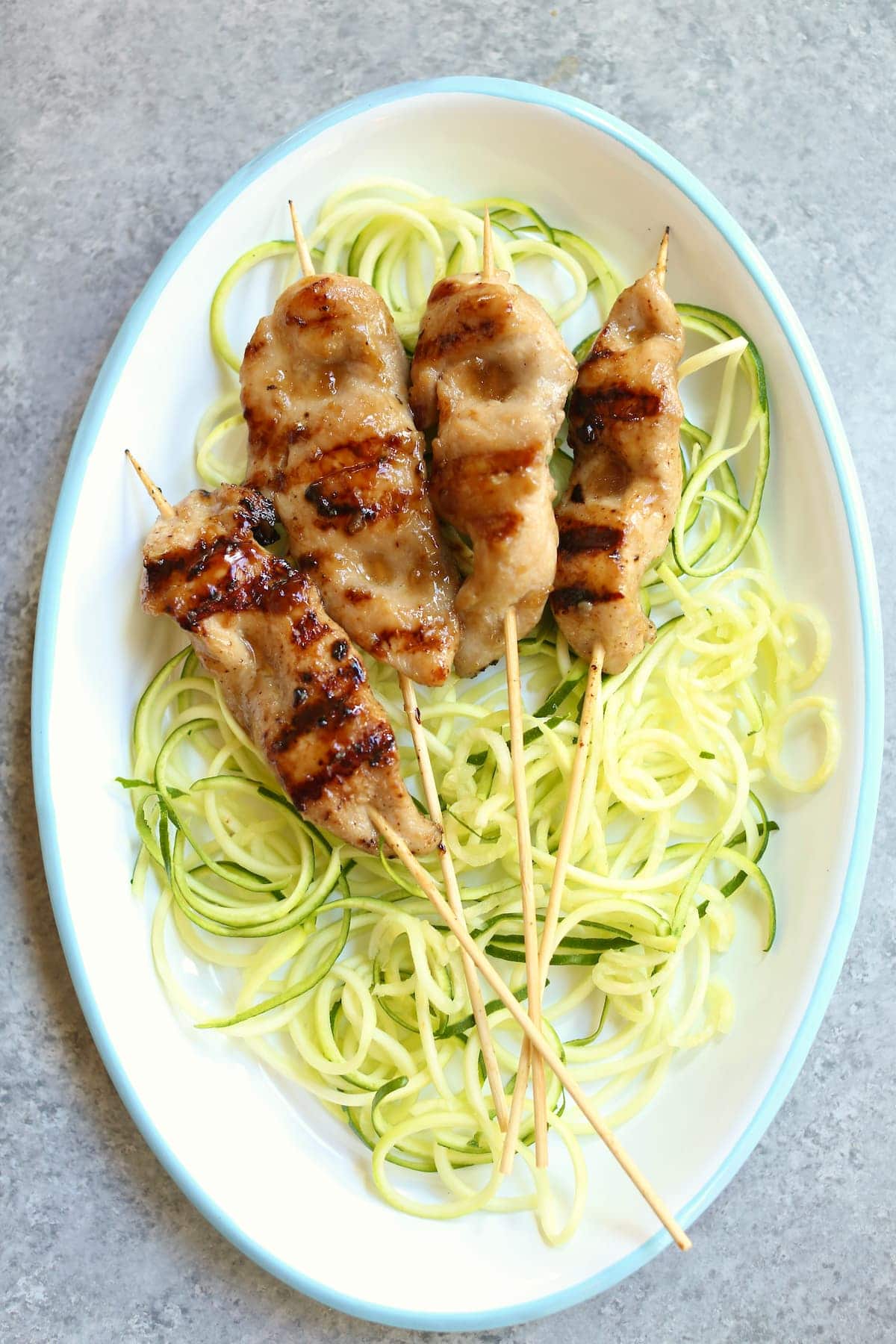 a white tray of chicken skewers with zucchini noodles.
