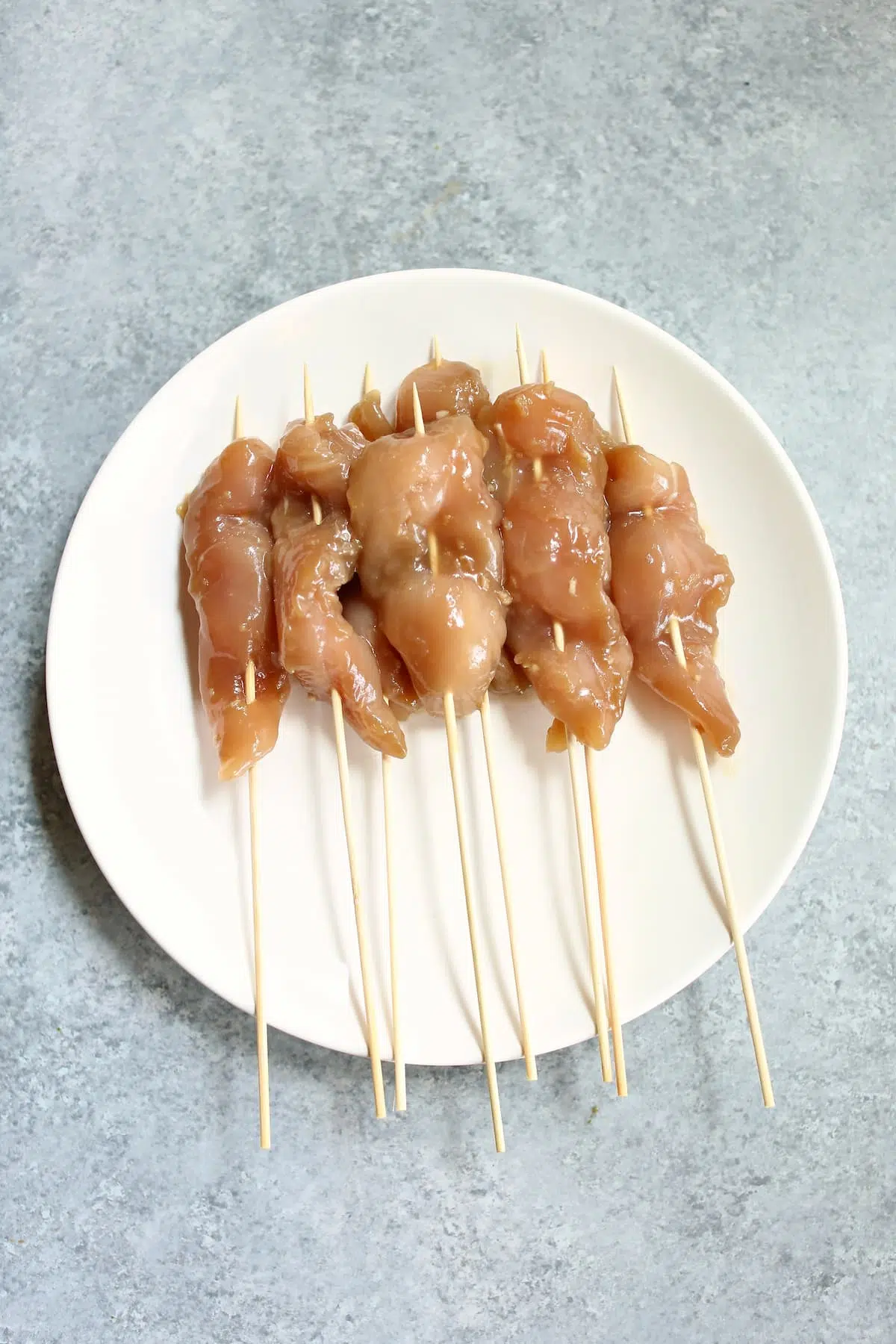 a white plate with uncooked chicken skewers on it.