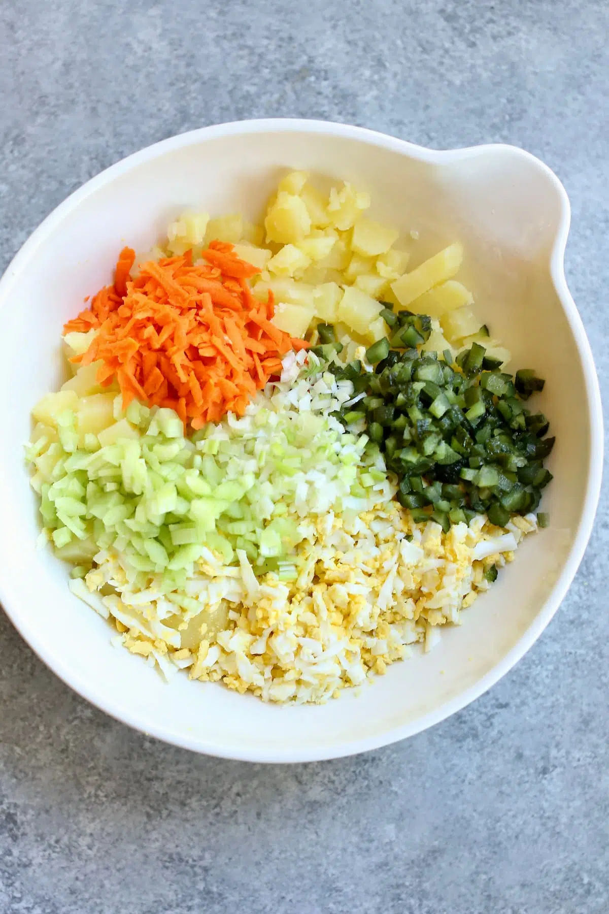 a white bowl with potato salad ingredients in it.