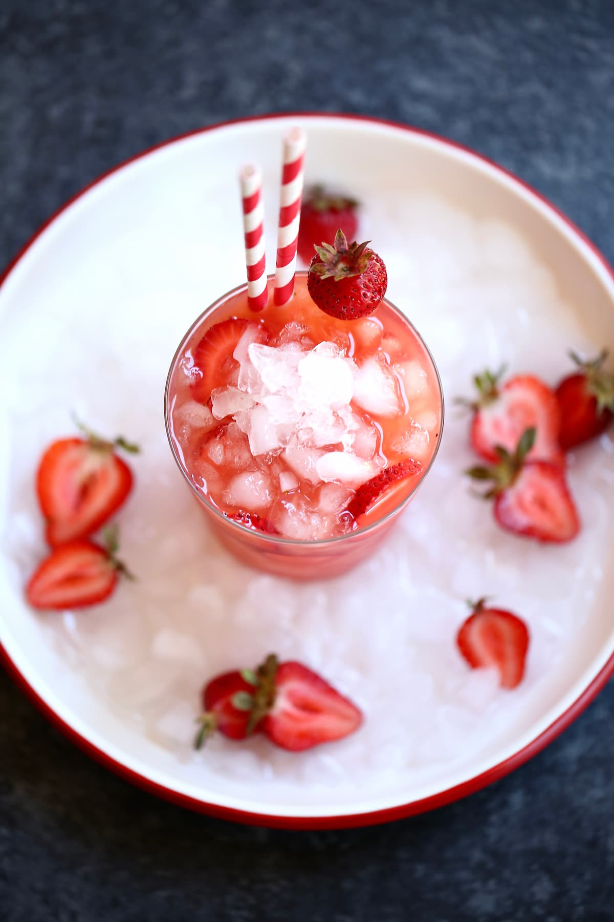 An overhead photo of a strawberry drink on a white plate with ice and sliced strawberries.