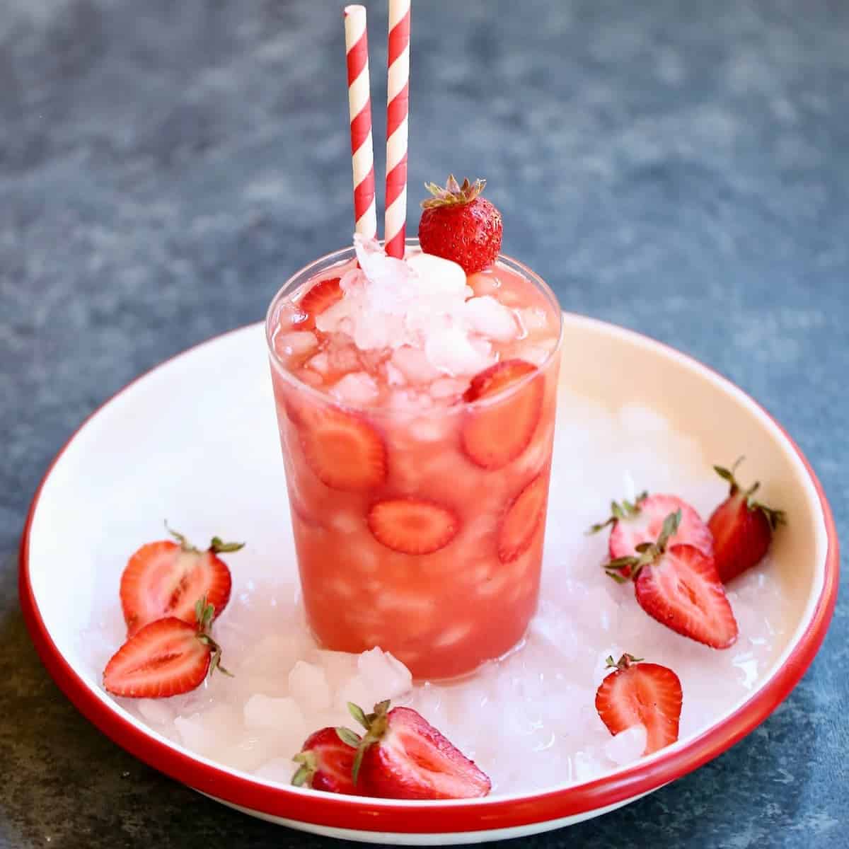 a white plate of a strawberry drink with ice.