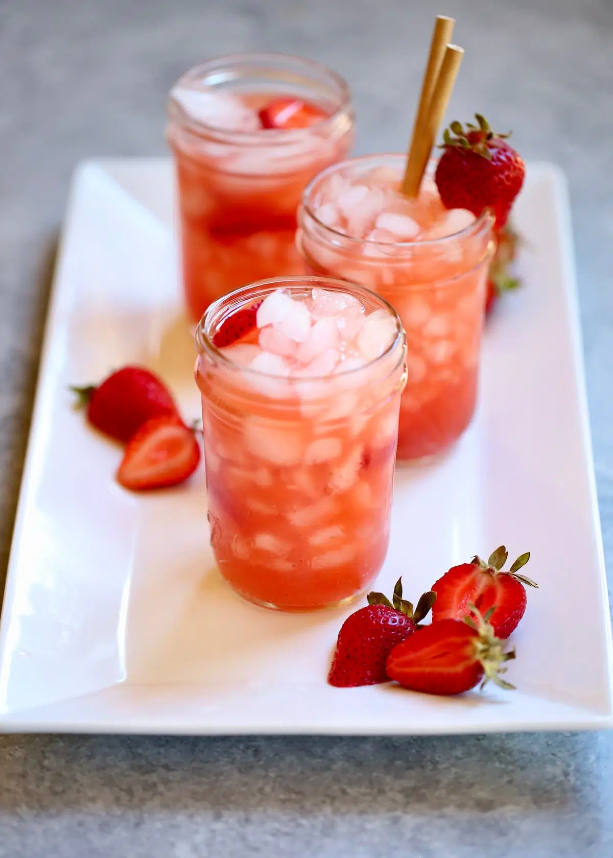 a white tray with three red strawberry drinks on it.