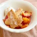 a white bowl of peach cobbler with text overlay.