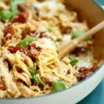 a photo of sun dried tomato pasta with a wooden spoon and text overlay with the recipe name.