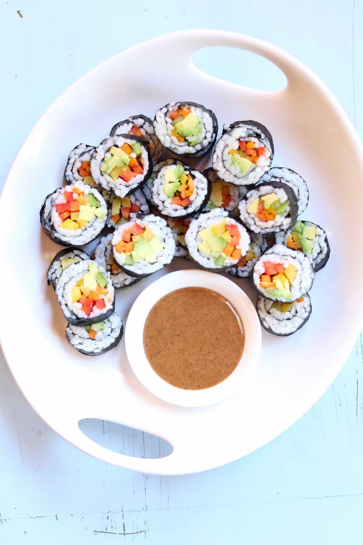 an overhead photo of veggie rolls on a white platter with peanut dipping sauce.
