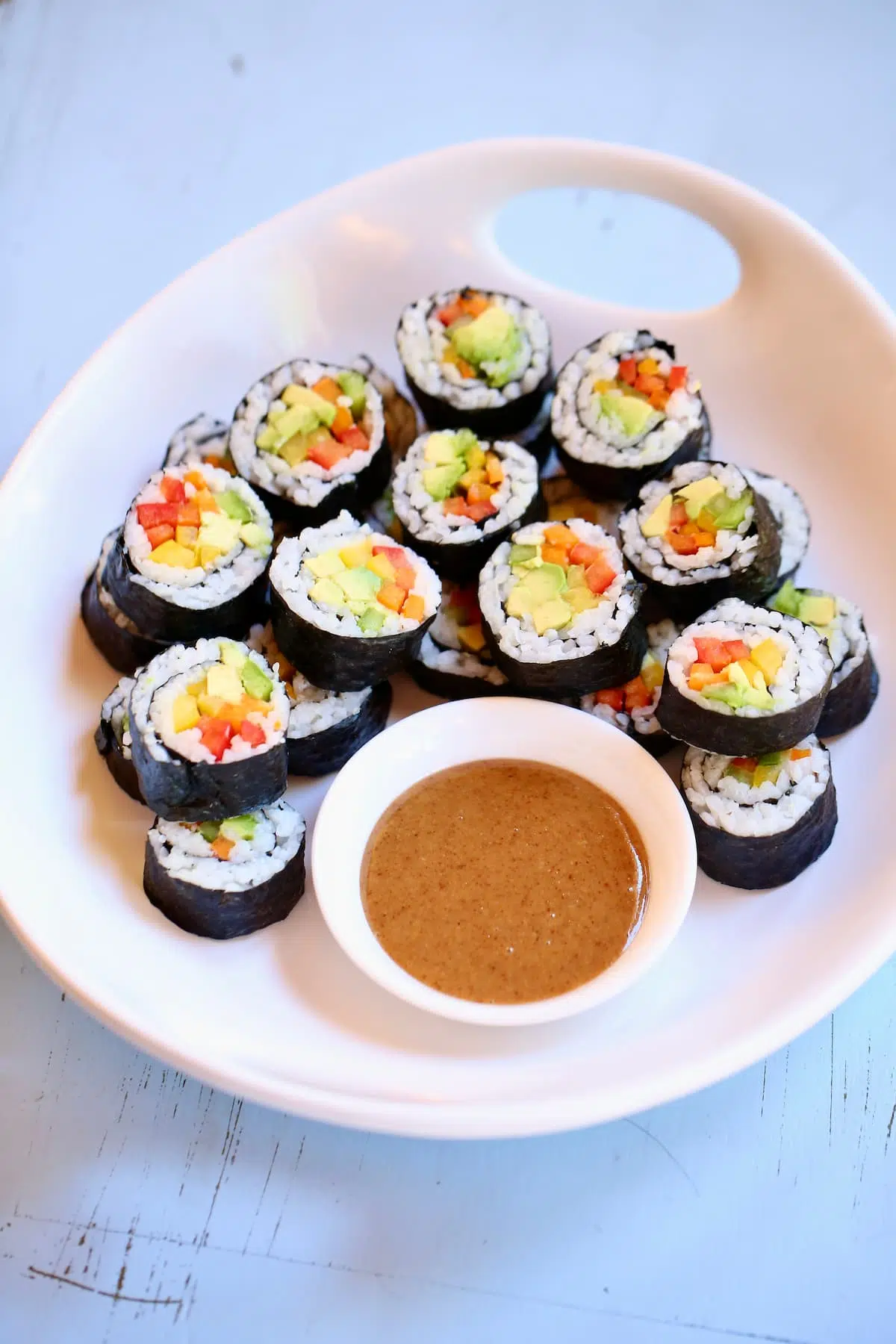 a white tray of veggie sushi rolls with dipping sauce.