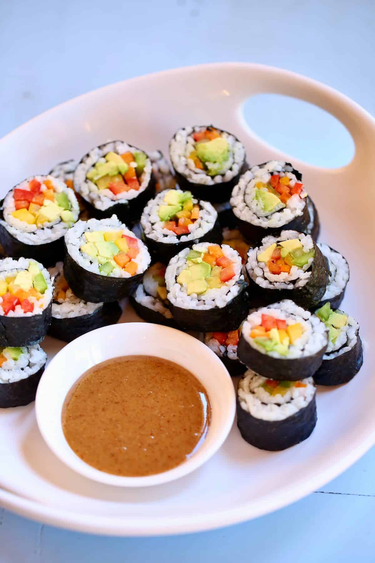 a close up photo of a platter of sushi rolls with dipping sauce.