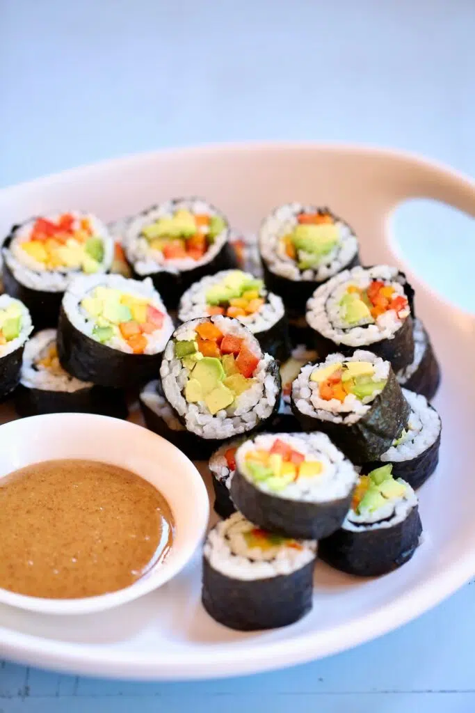 a white tray of avocado rolls with a side of sauce.