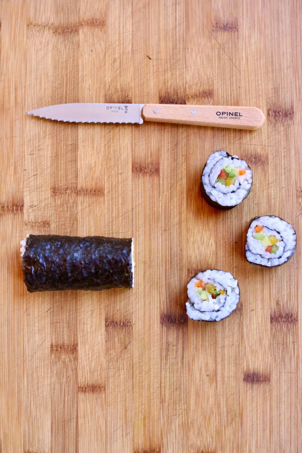 a cutting board with a sushi roll with slices made, and a knife.
