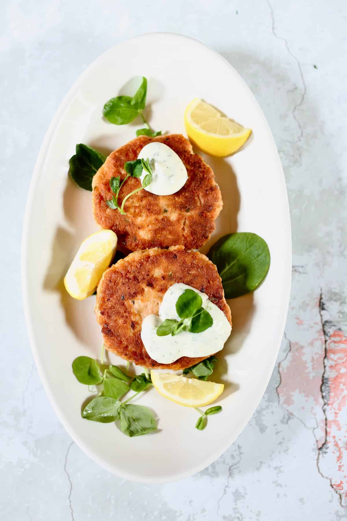 a white platter of salmon patties with dill sauce.