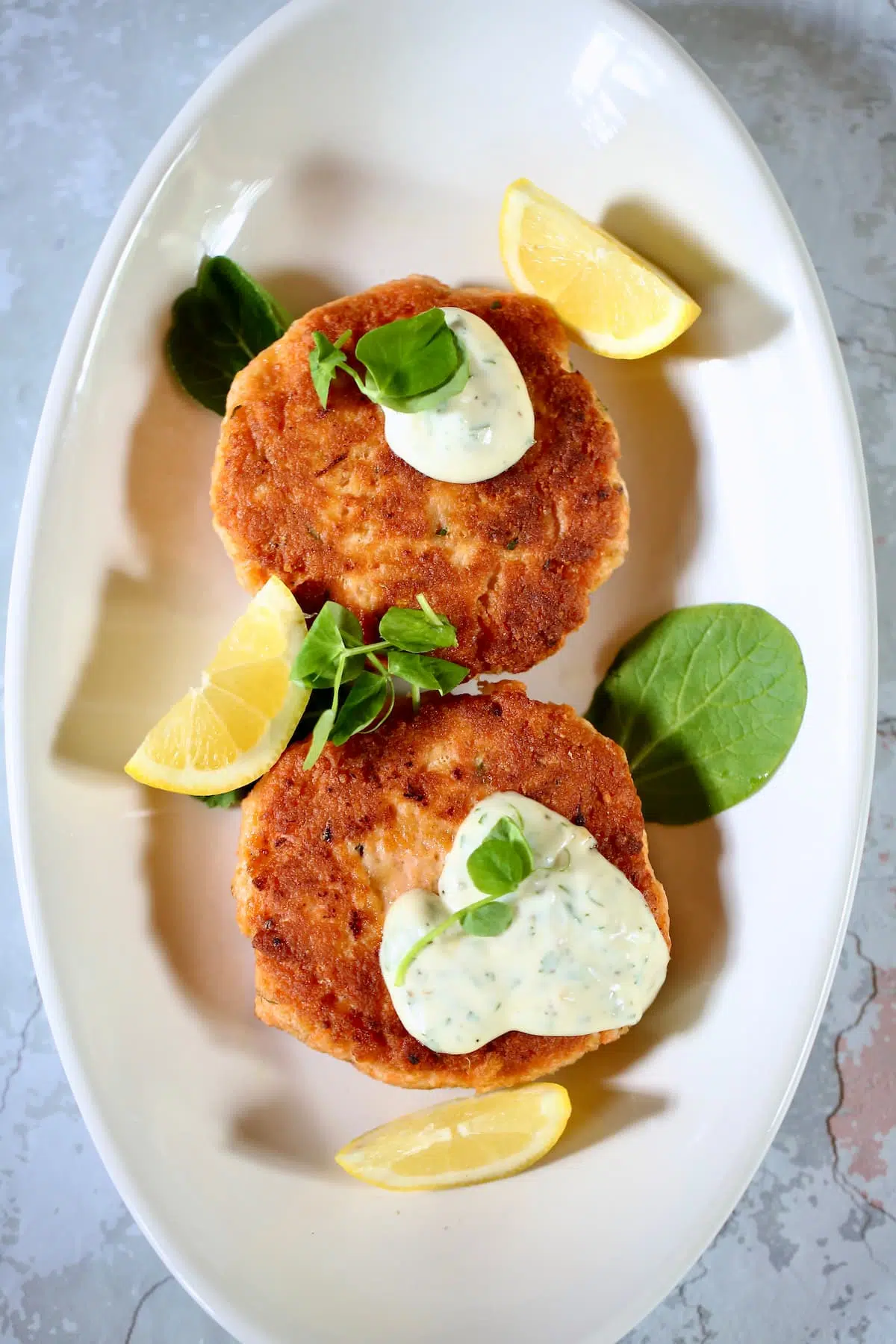 a white platter with two salmon patties on it and dill sauce.