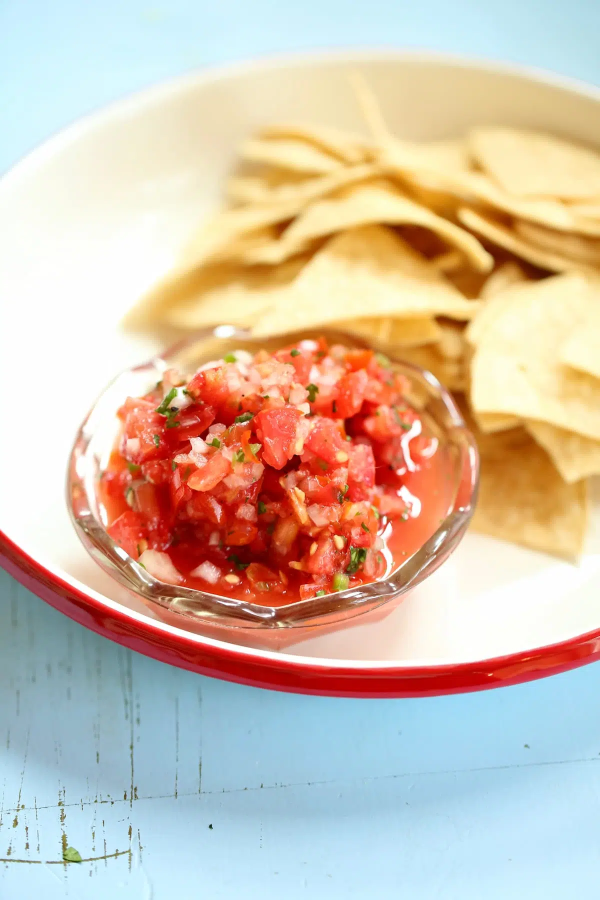 a bowl of salsa on a white platter with chips behind it.