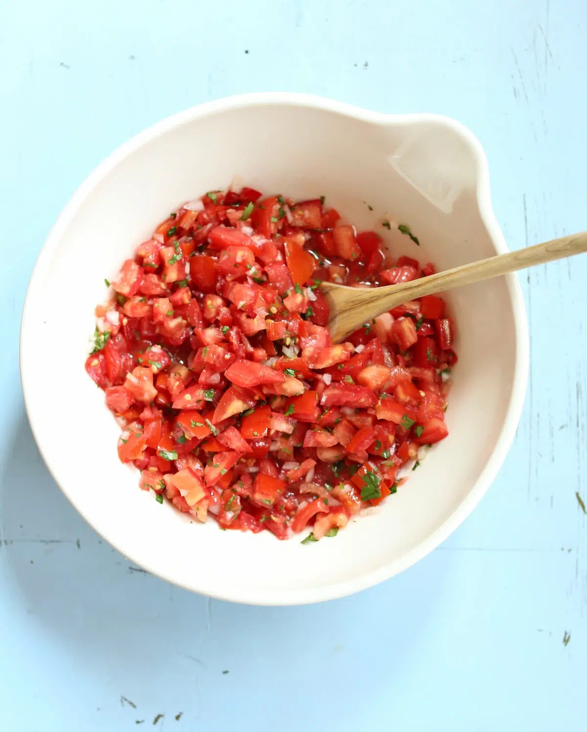 a white bowl on a blue table with salsa in it and a wooden spoon.