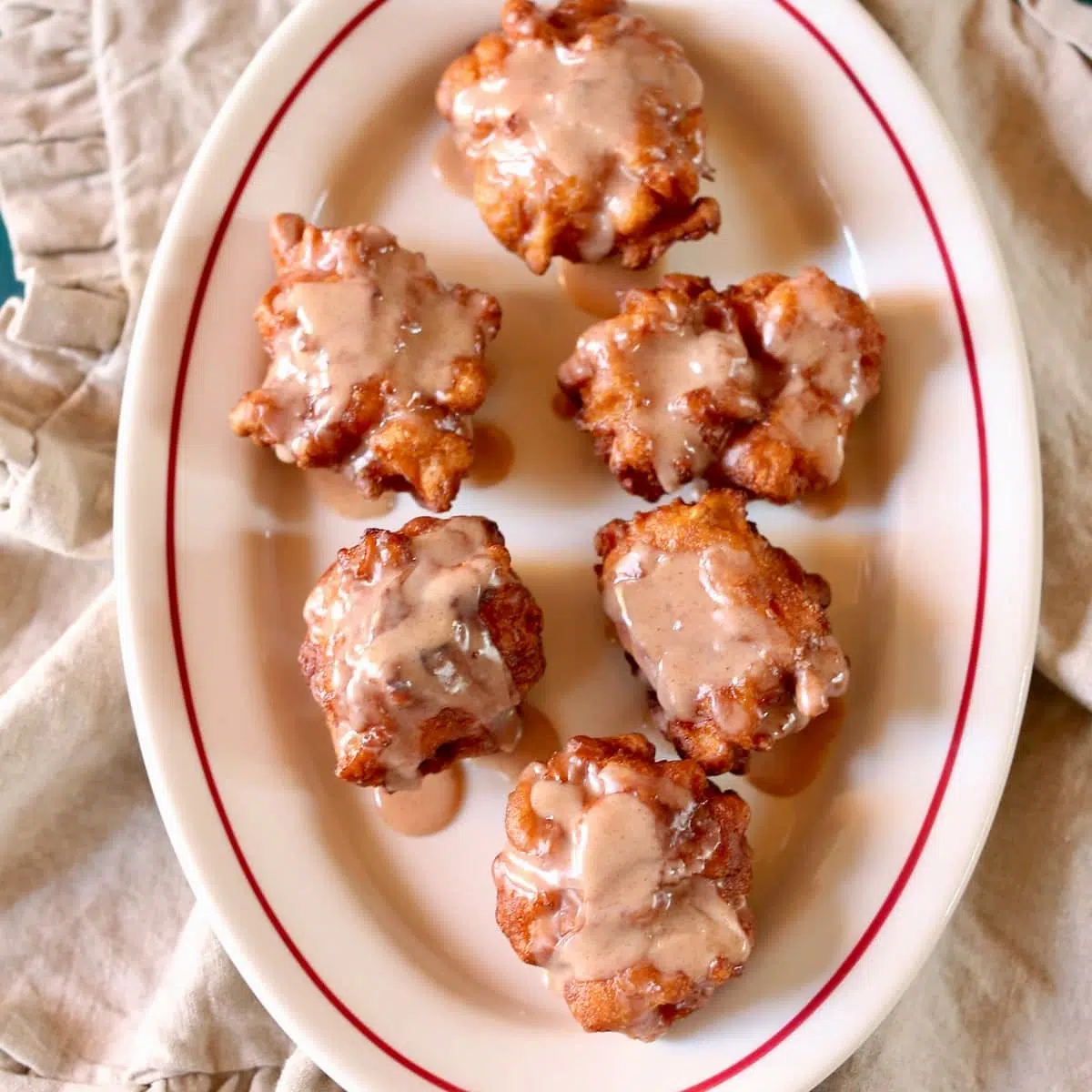 a square photo of an overhead of apple fritters on a white platter.