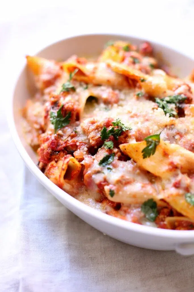 a white platter with baked pasta and chicken sausage.