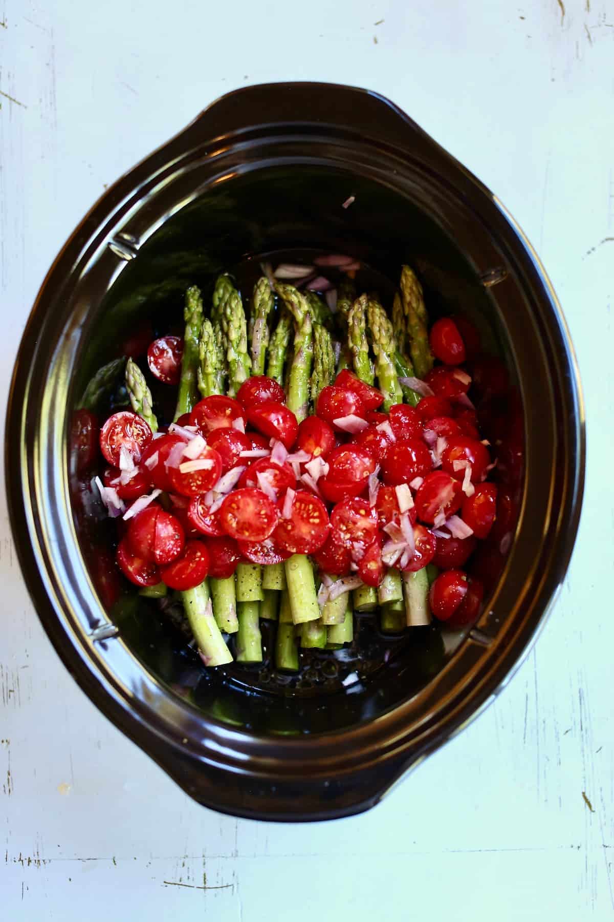 an overhead photo of a slow cooker with asparagus in it and tomatoes.