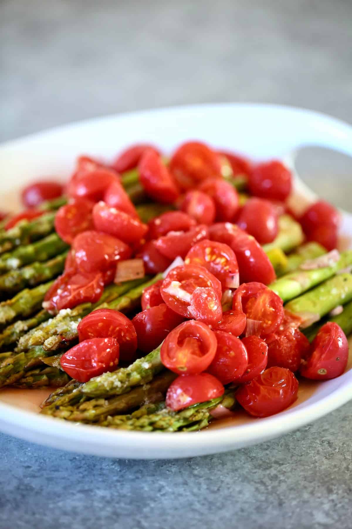 a side view of asparagus with tomatoes on top.  