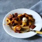 a waffle on a plate with pecans and syrup.