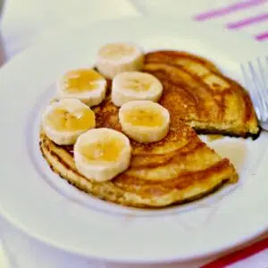 a white plate of pancakes with bananas.