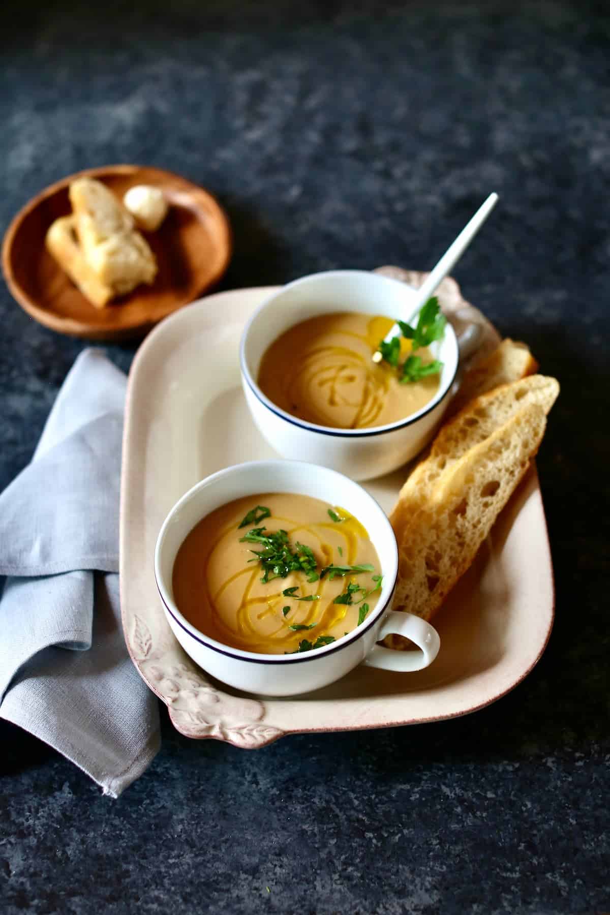 a photo of two cups of soup on a tray with a plate of bread.