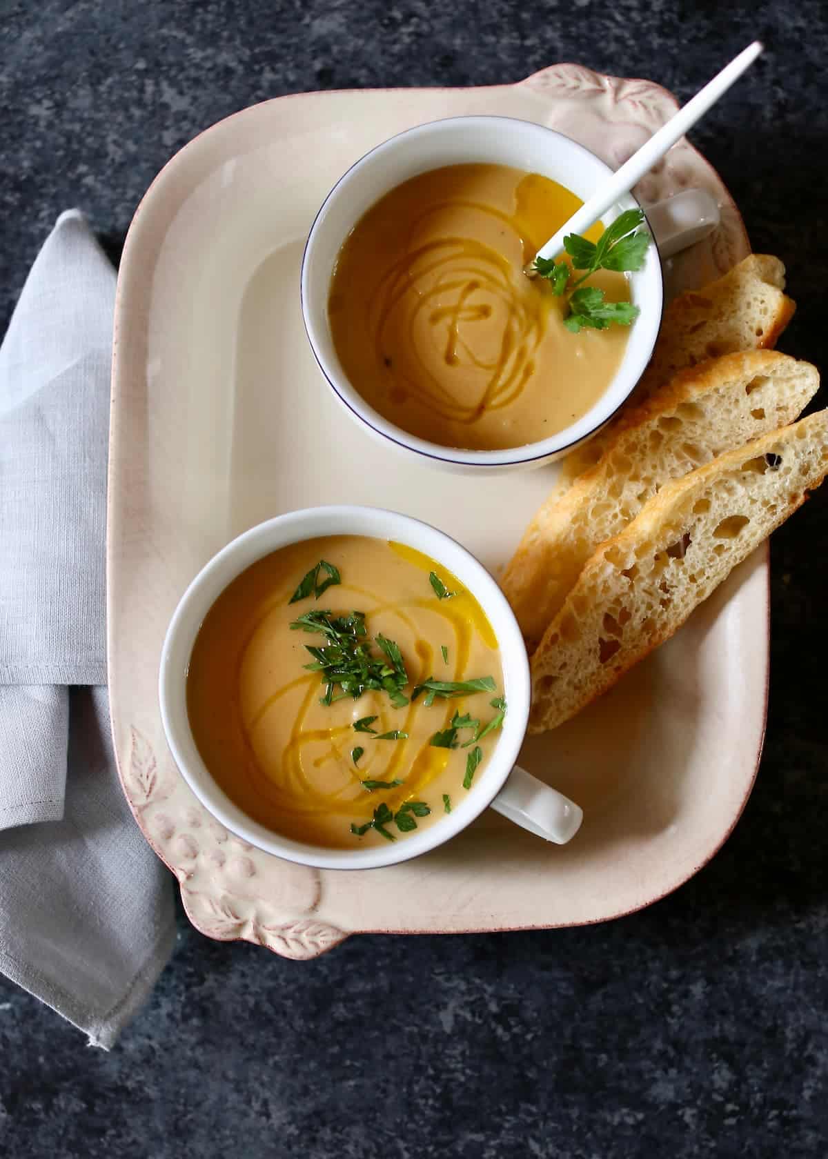 a tray with two cups of soup and bread on it.