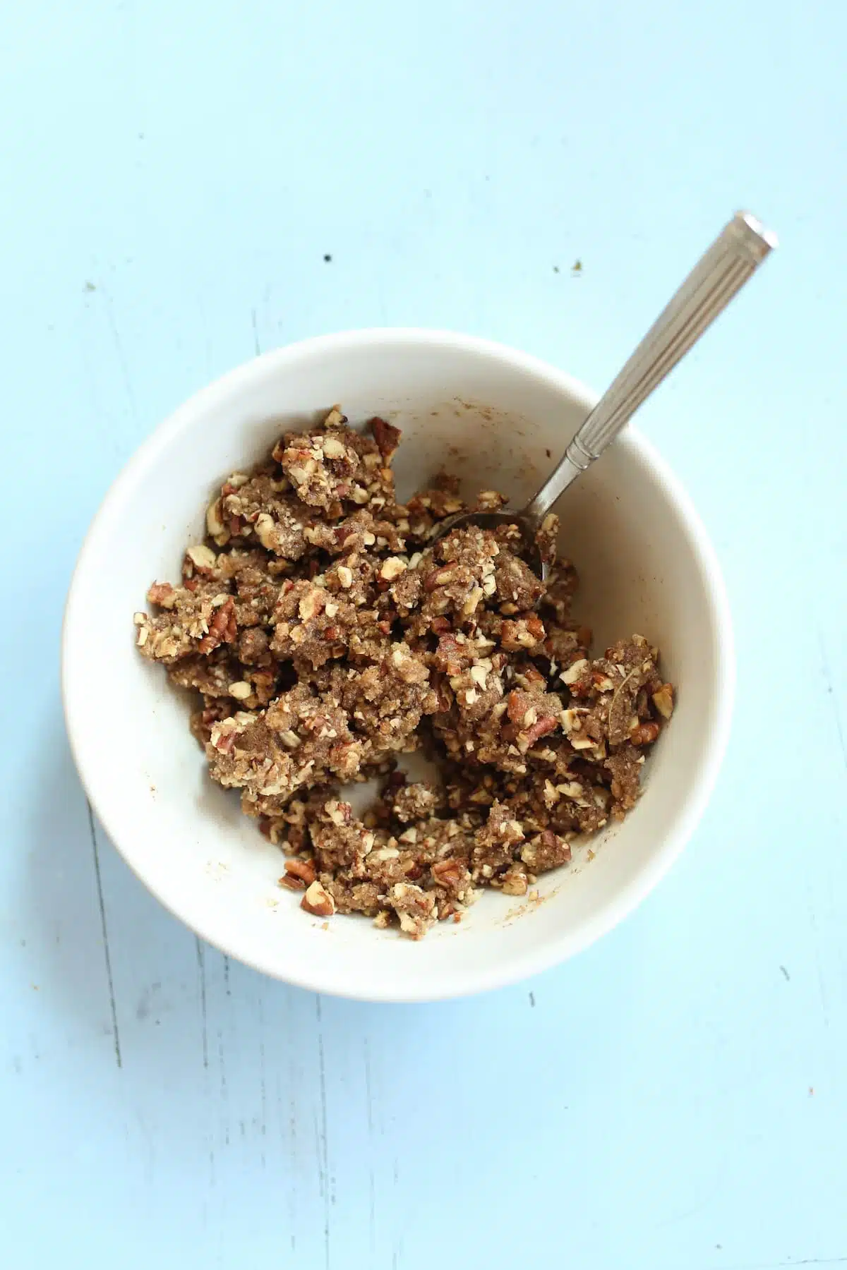 an overhead photo of a crumble topping in a white bowl with a spoon out the side.
