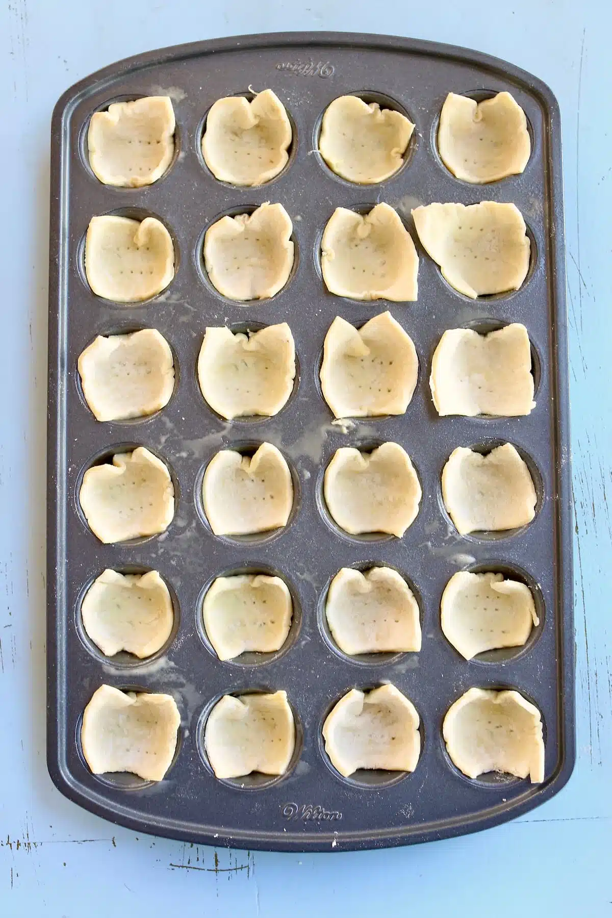 a baking sheet of puff pastry cups ready to be filled with cheese.