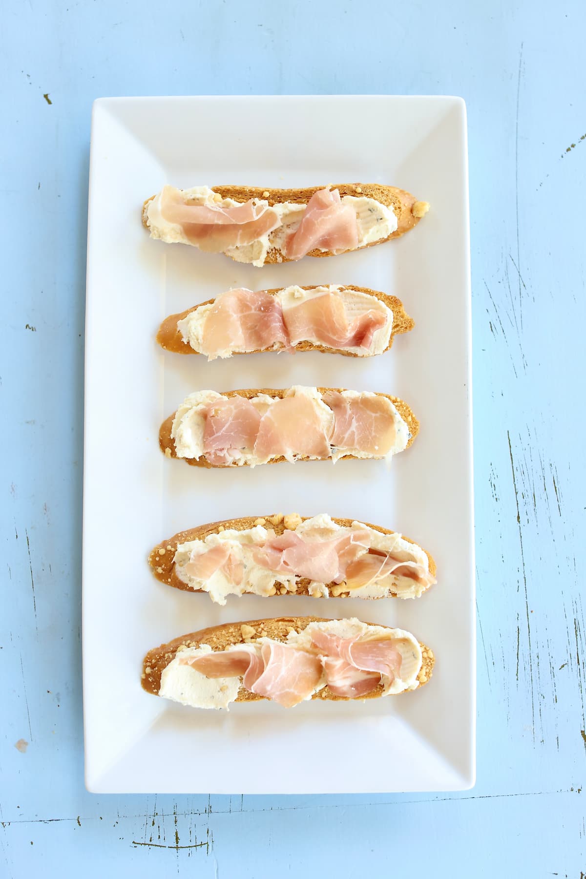 an overhead photo of prosciutto toasts on a white platter.