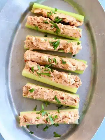 a silver platter of stuffed celery on a blue table.