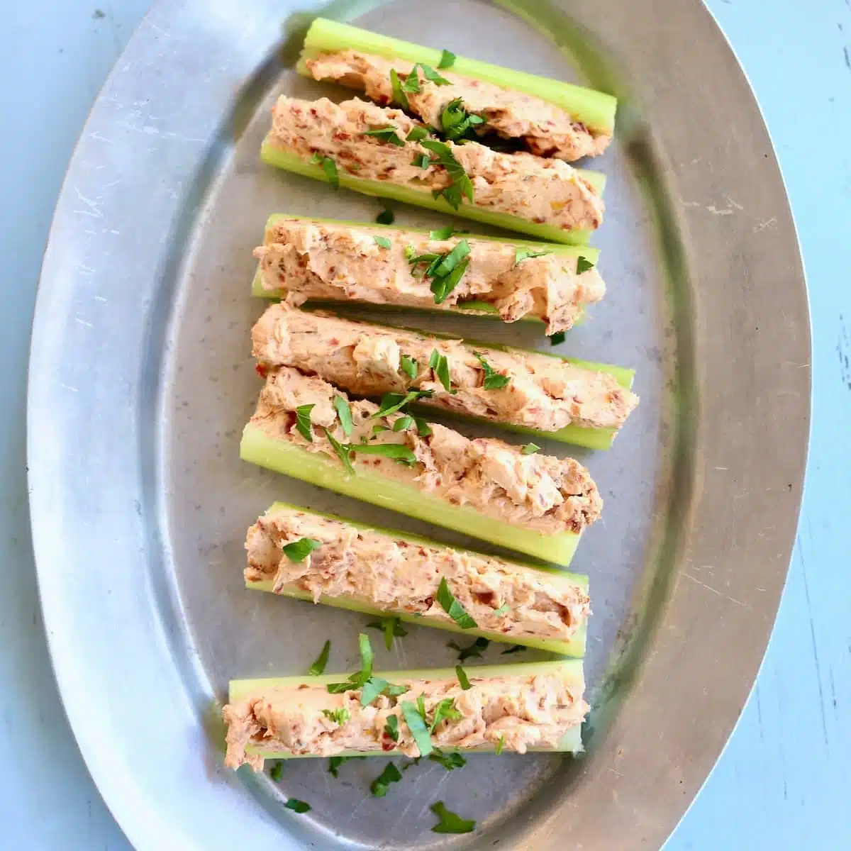 a silver platter of stuffed celery on a blue table.