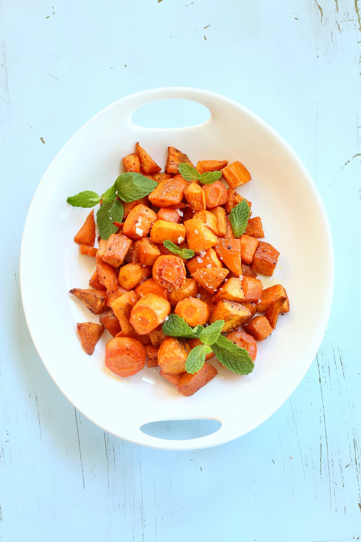 an overhead photo of carrots and sweet potatoes in a white bowl on a blue table.