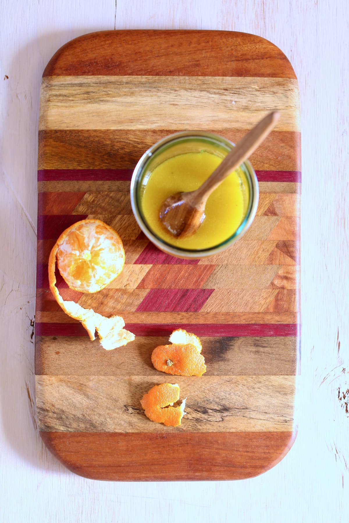 a cutting board with a jar of vinaigrette on it and an orange.