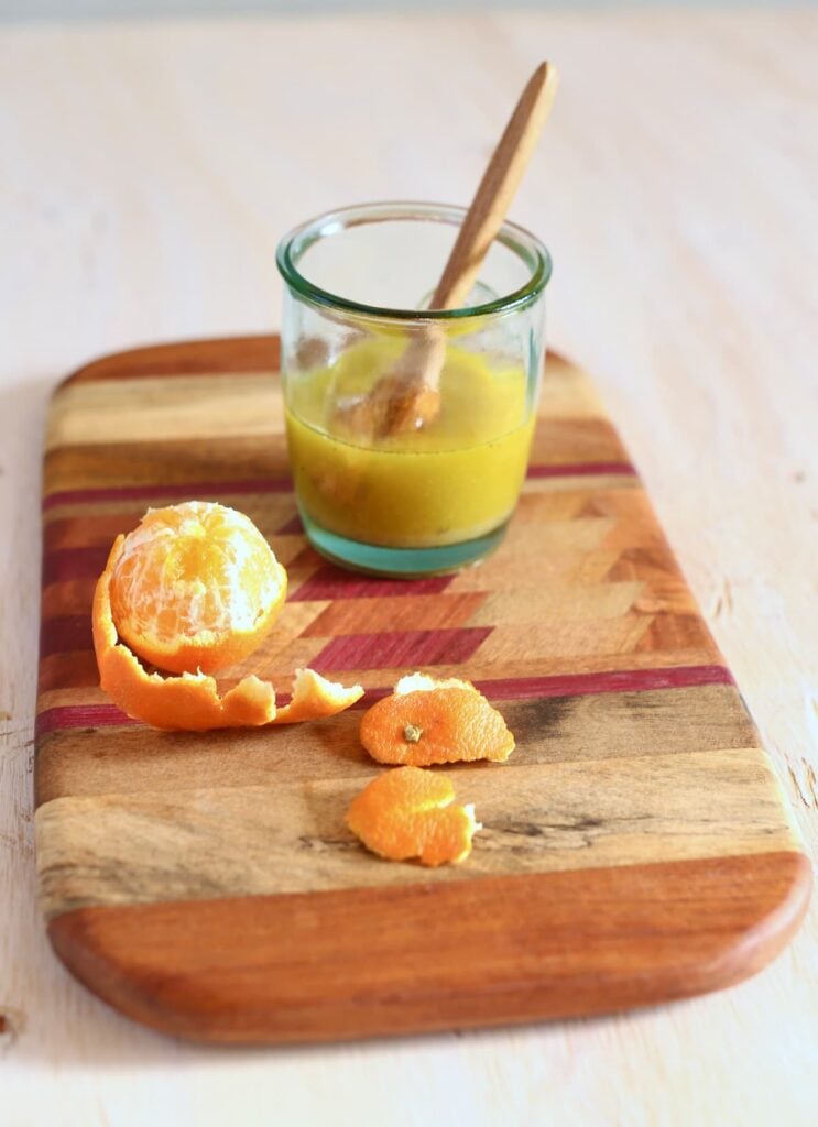 a cutting board with vinaigrette in a small jar with an orange next to it.