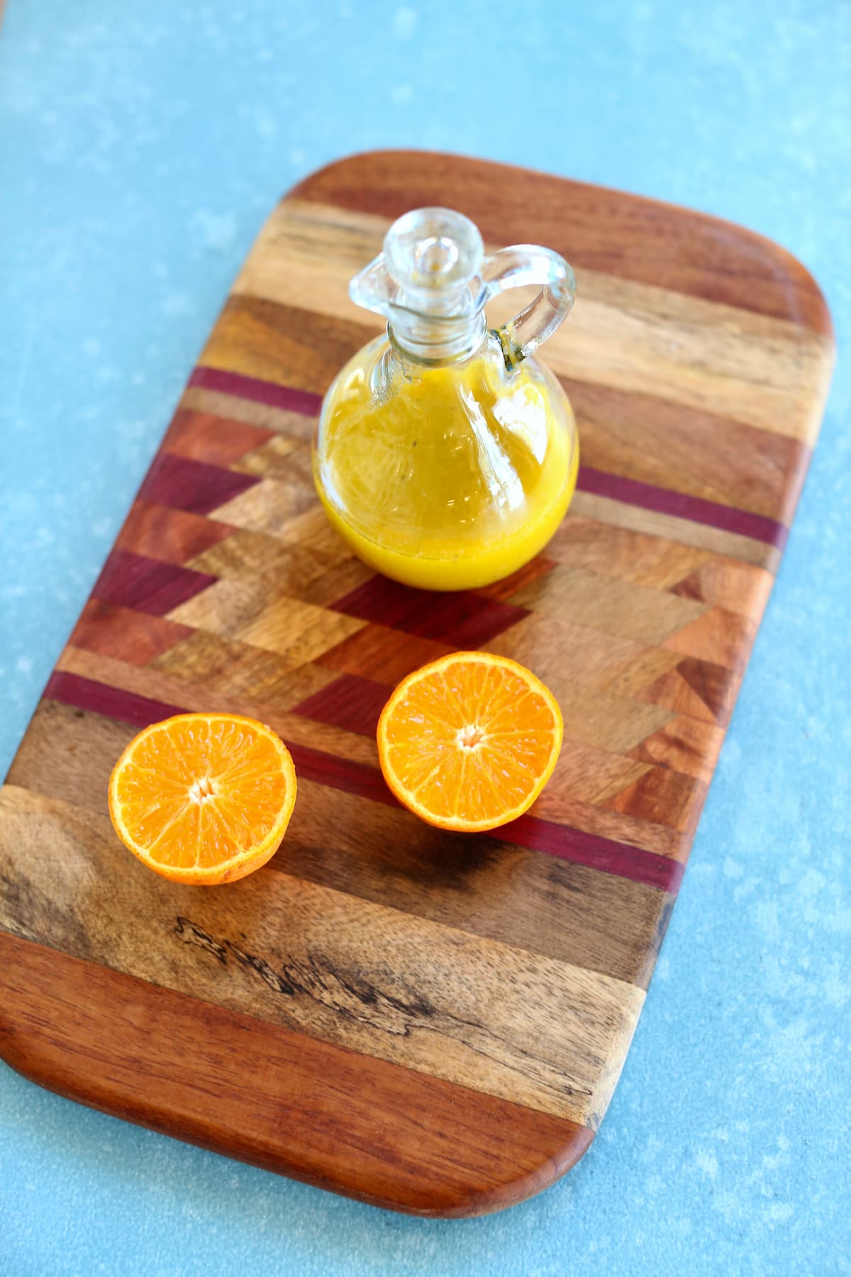 a cutting board with a bottle of vinagrette and an orange on it.