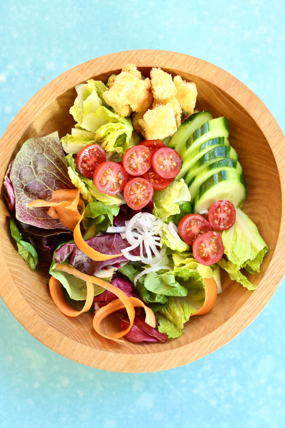 an overhead photo of a green salad in a wooden bowl.