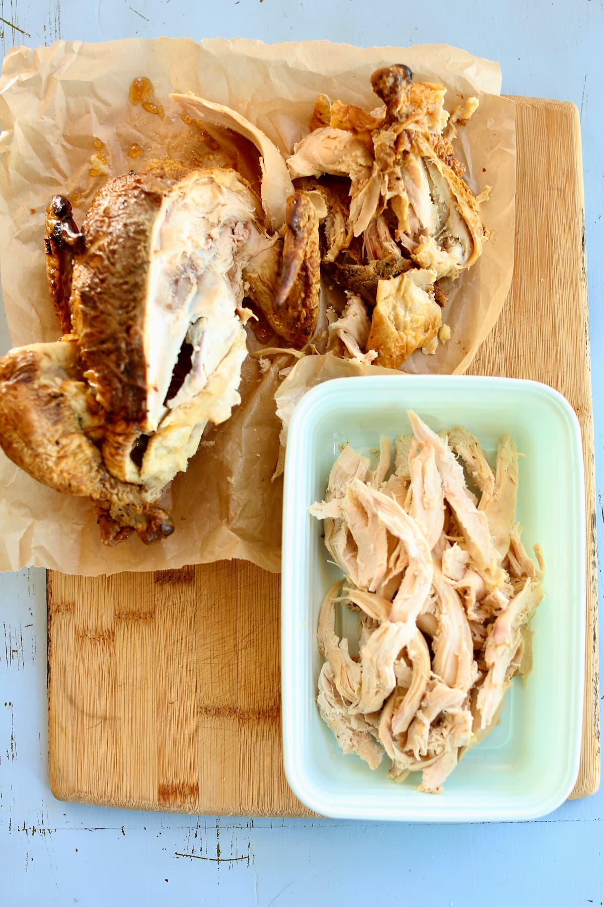 a cutting board of a whole chicken and shredded chicken.