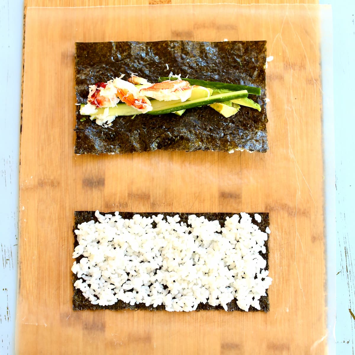 A cutting board with two sushi rolls on it, laying flat on the board.