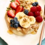 a close up photo of naan breakfast pizza with nut butter and berries.