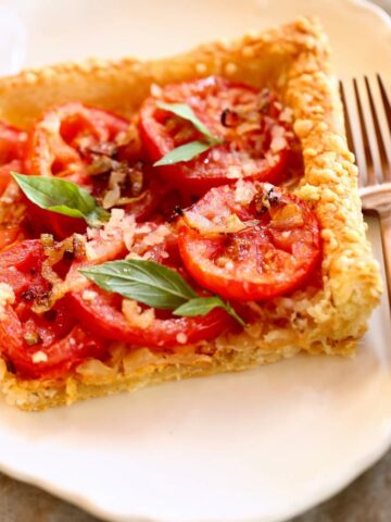 a square image of a tomato tart on a plate with fork.