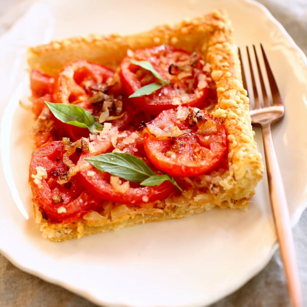 a square image of a tomato tart on a plate with fork.