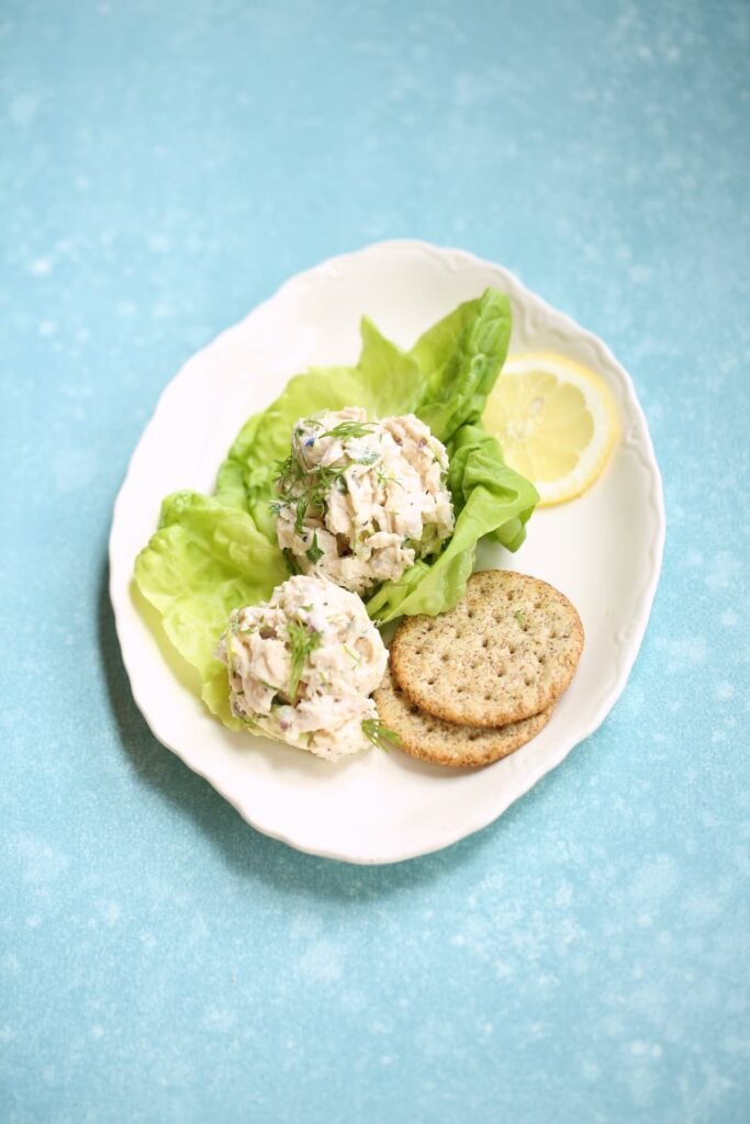 A white plate with chicken salad in lettuce cups with crackers, ready for serving.